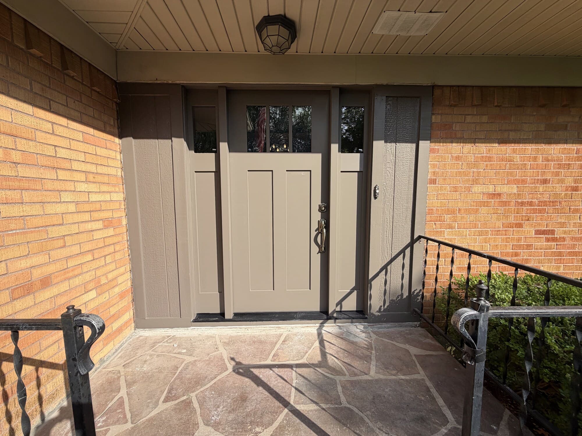 Taupe craftsman-style front door with three-lite glass and matching sidelights, set in a brick ranch entry under a covered porch