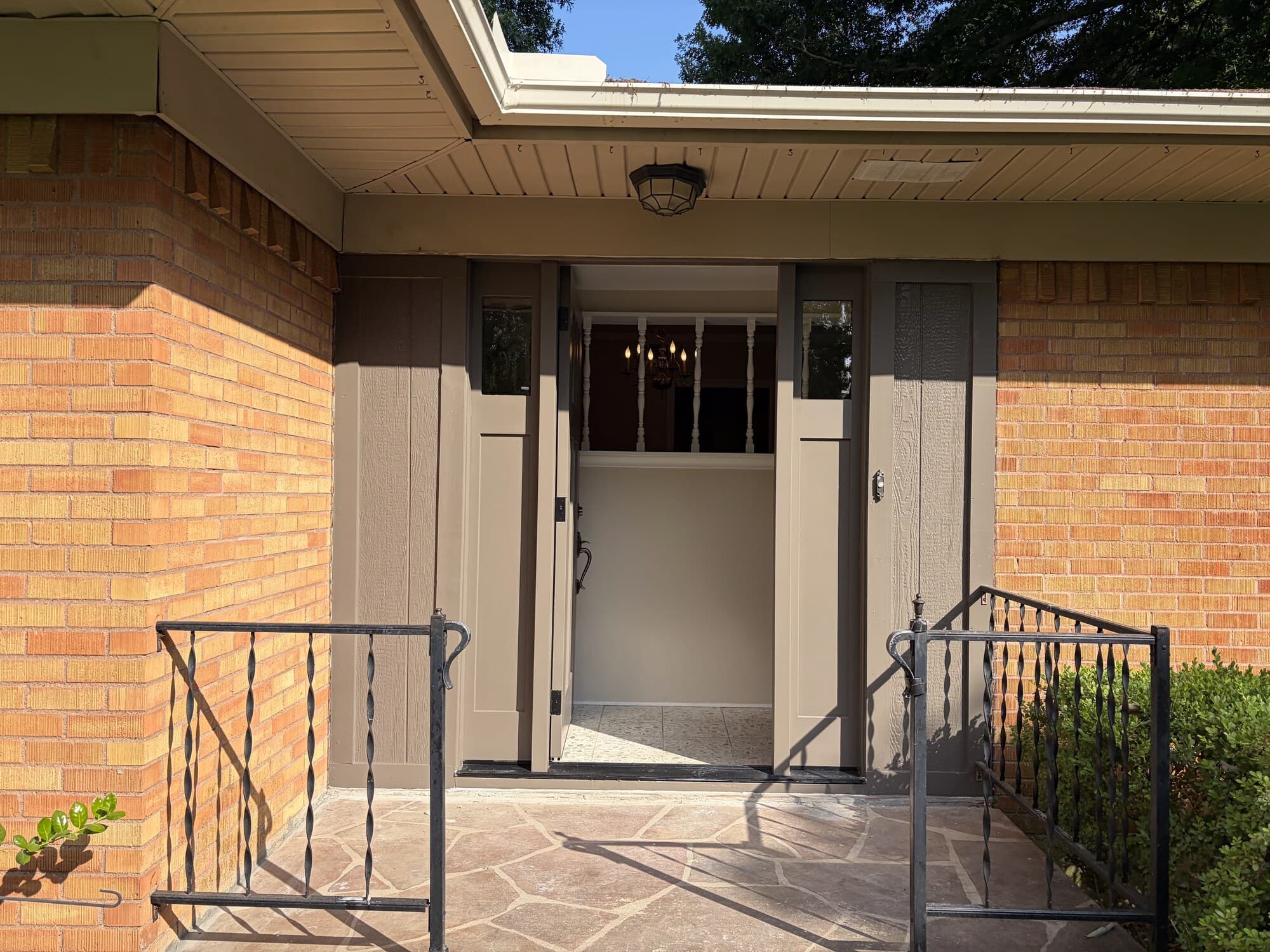 The new front door standing open, seen from the covered porch, with wrought-iron railings and flagstone
