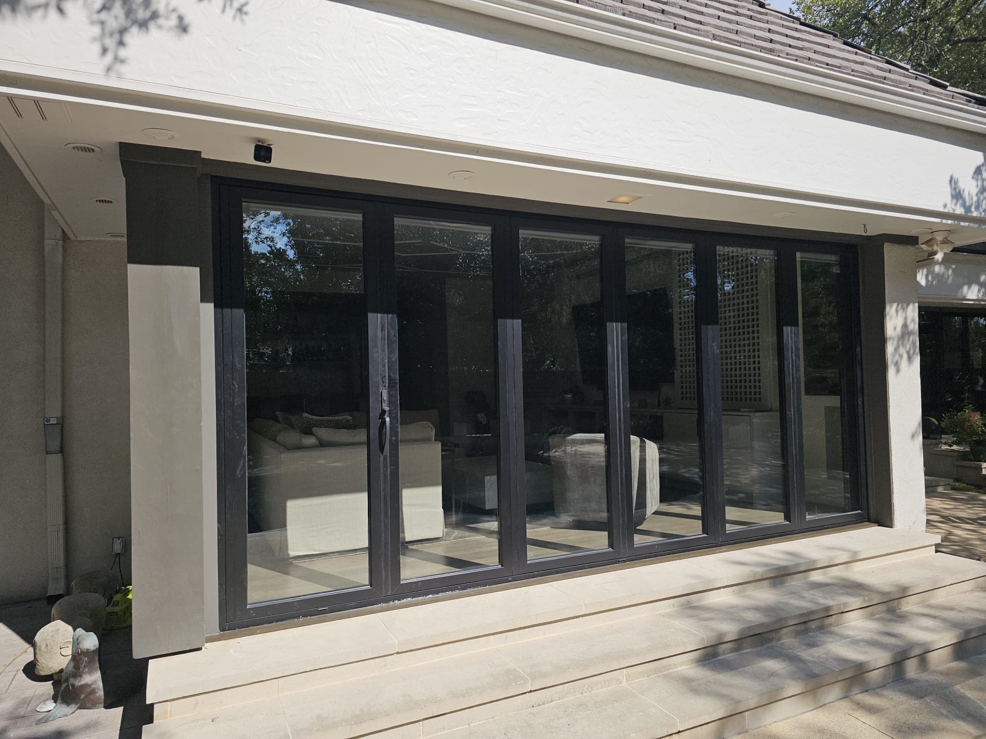 Multi-panel black-framed sliding door system seen from outside, closed, running the length of a stucco elevation