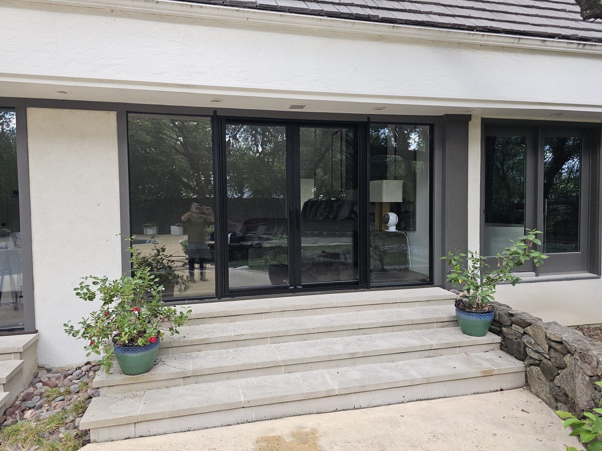 Wide black-framed multi-slide opening spanning most of a stucco elevation, above wide stone steps with planters
